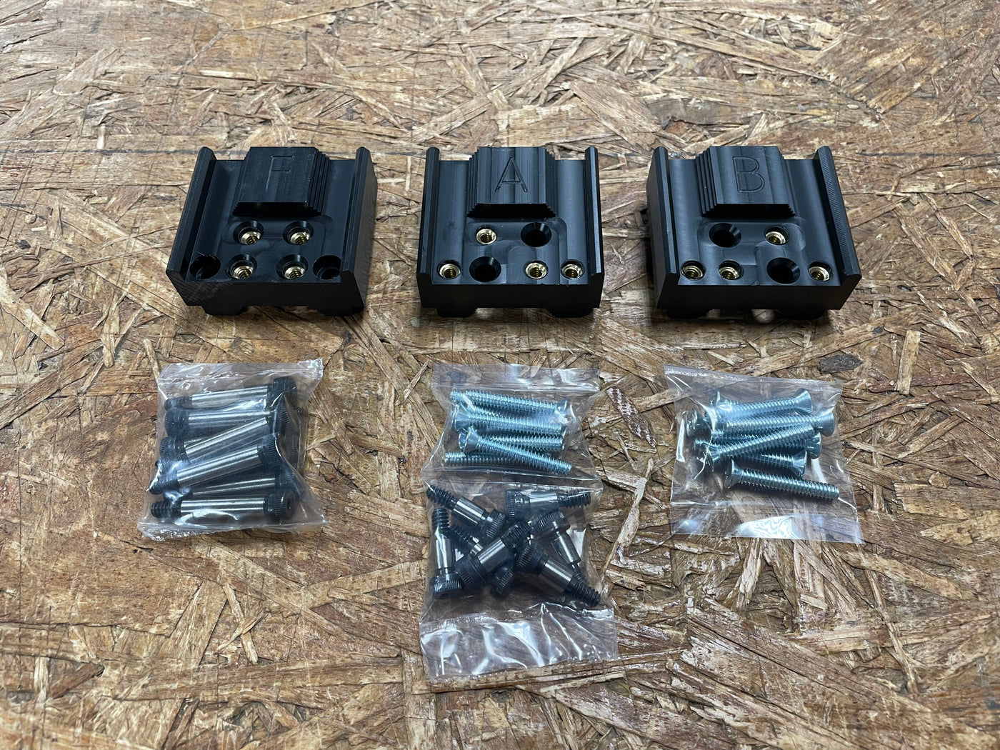 Three black plastic components with screws on a wooden surface